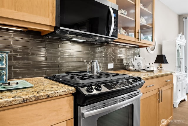 kitchen featuring light stone counters, glass insert cabinets, appliances with stainless steel finishes, and light brown cabinets