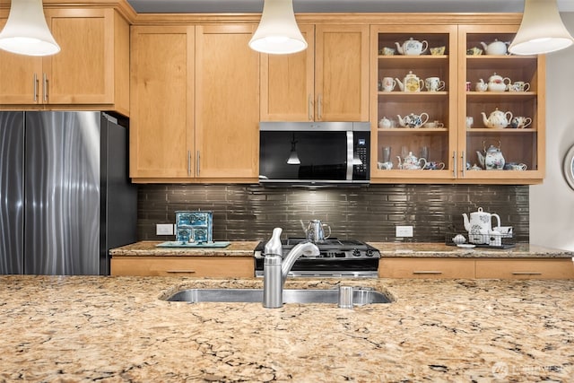 kitchen with a sink, stainless steel appliances, light stone countertops, and backsplash