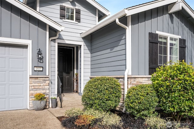 view of exterior entry with stone siding, board and batten siding, and a garage