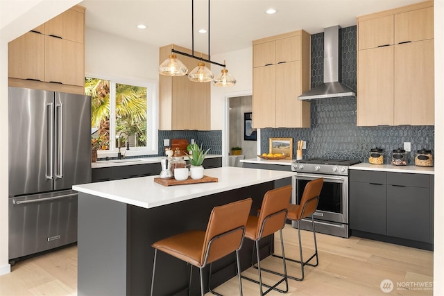 kitchen featuring light brown cabinets, appliances with stainless steel finishes, wall chimney exhaust hood, and a sink