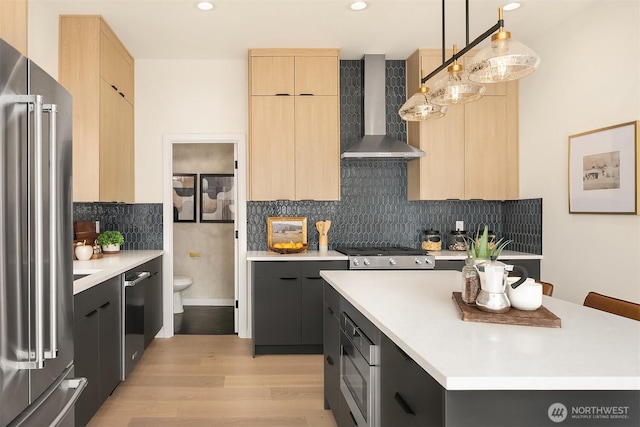 kitchen with stainless steel appliances, light brown cabinets, and wall chimney range hood