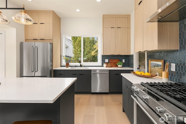 kitchen with under cabinet range hood, modern cabinets, light brown cabinets, and appliances with stainless steel finishes