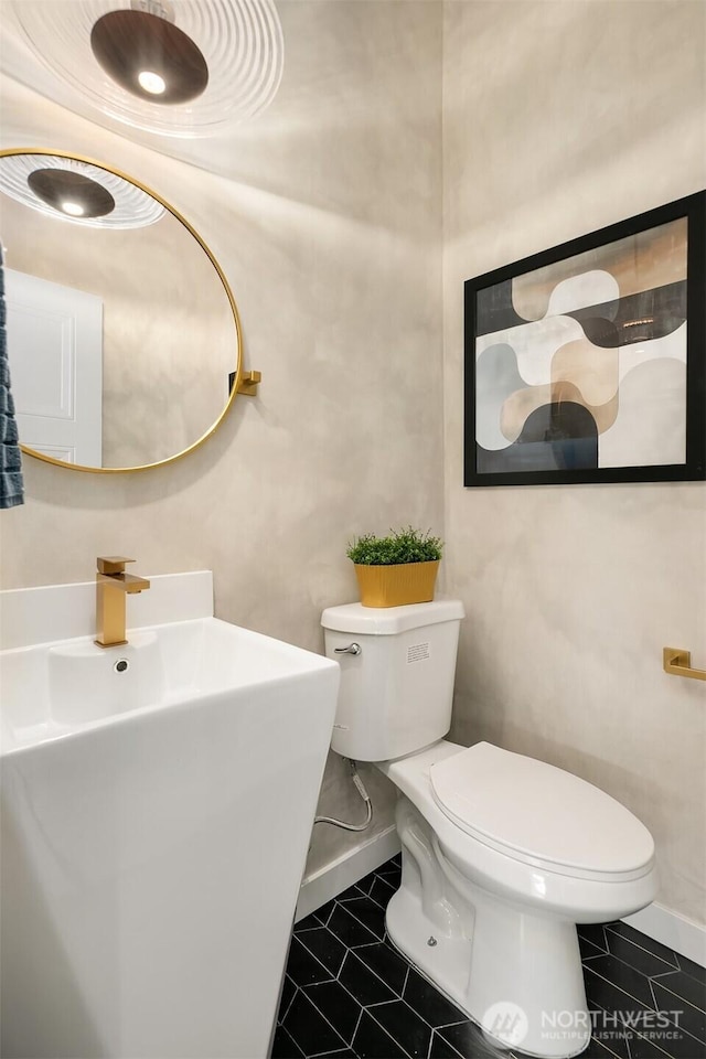 half bathroom featuring toilet, baseboards, and a sink