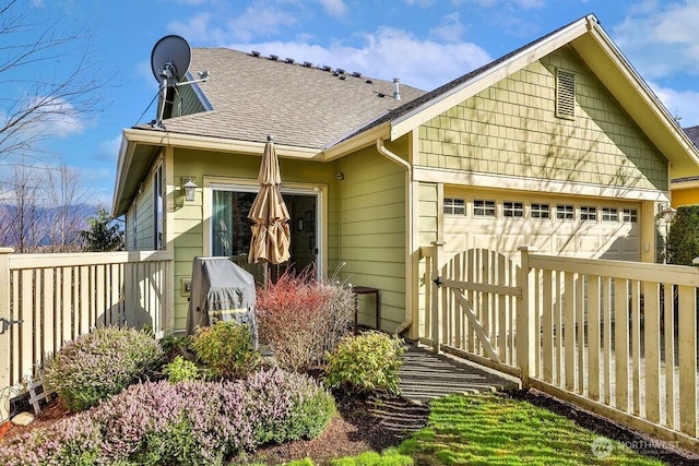 exterior space featuring an attached garage, a shingled roof, and fence