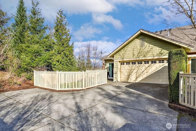 view of side of property featuring concrete driveway, fence, and a garage