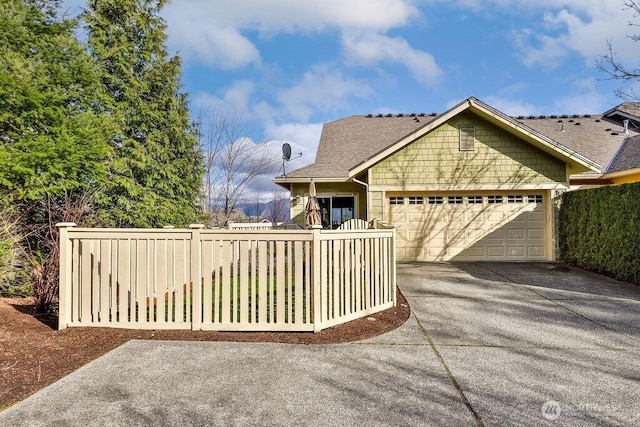 view of front of house with driveway, roof with shingles, a garage, and fence