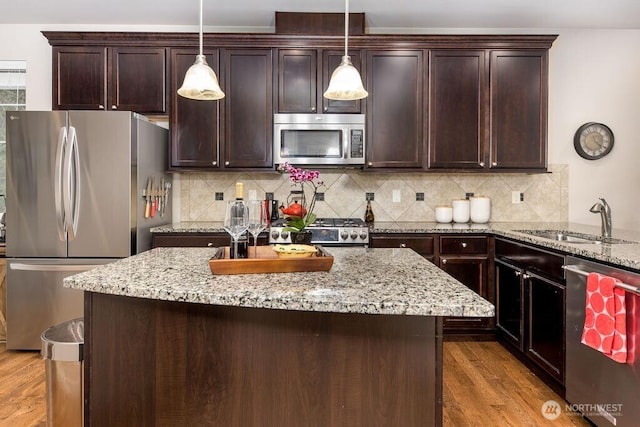 kitchen featuring light stone countertops, dark brown cabinetry, appliances with stainless steel finishes, wood finished floors, and a sink