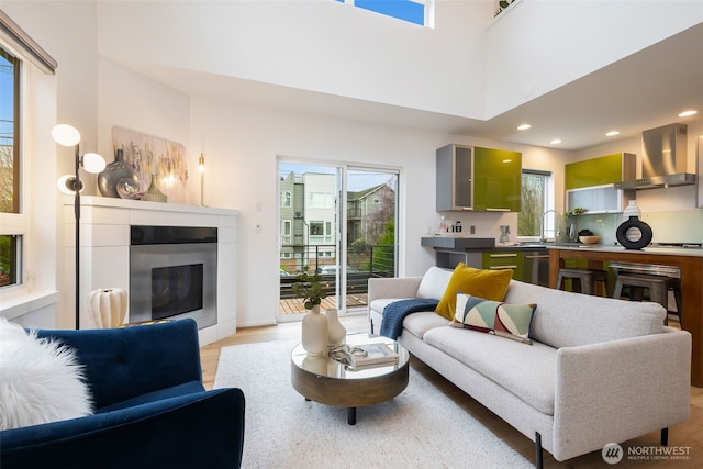 living room featuring recessed lighting, light wood-style floors, a high ceiling, and a glass covered fireplace