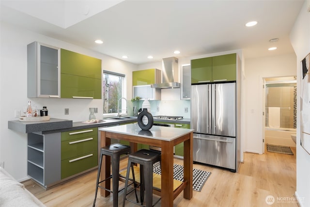 kitchen with green cabinets, wall chimney exhaust hood, light wood-style floors, and stainless steel appliances