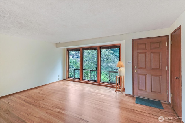 foyer featuring light wood-style flooring, visible vents, baseboards, and a textured ceiling