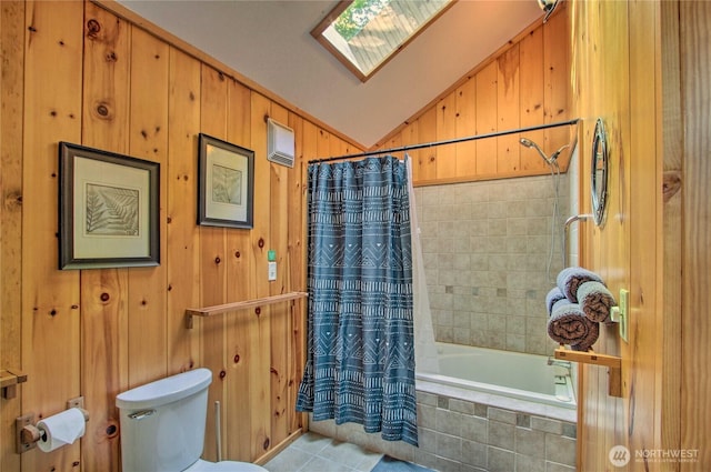 bathroom featuring lofted ceiling with skylight, wood walls, toilet, tiled shower / bath combo, and tile patterned floors