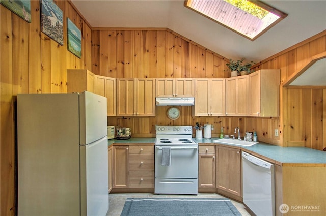 kitchen with wooden walls, under cabinet range hood, vaulted ceiling with skylight, white appliances, and a sink