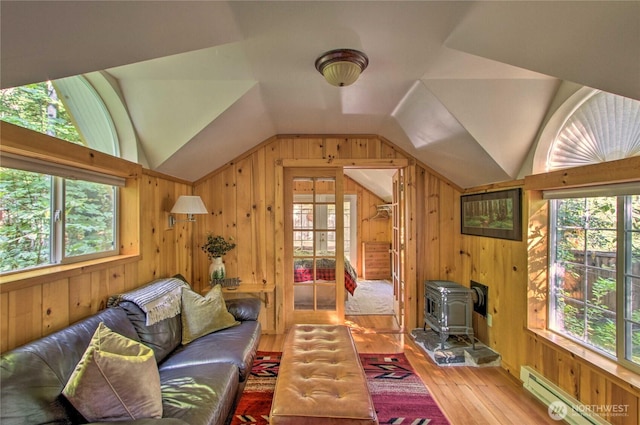 living room with wooden walls, lofted ceiling, hardwood / wood-style floors, a wood stove, and a baseboard radiator