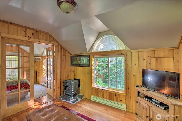 living room featuring lofted ceiling, a wood stove, light wood-type flooring, and a baseboard radiator