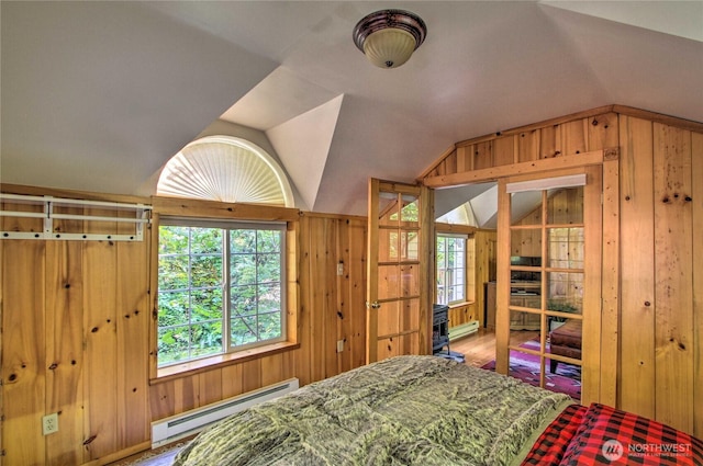 bedroom featuring wooden walls, baseboard heating, multiple windows, and lofted ceiling