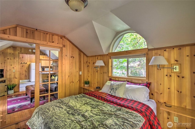 bedroom with lofted ceiling, wooden walls, wood-type flooring, and freestanding refrigerator