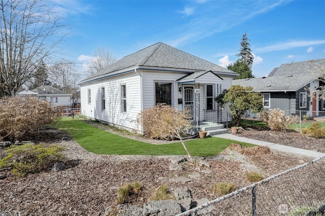 view of front of property featuring a front lawn, fence, and roof with shingles