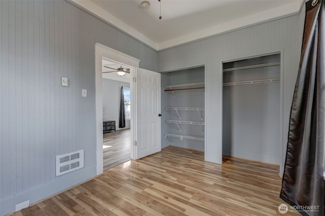 unfurnished bedroom featuring light wood-style floors, visible vents, and two closets