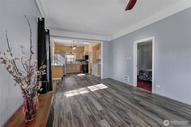 unfurnished living room with dark wood finished floors, visible vents, baseboards, and ceiling fan