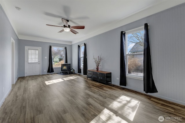 interior space with baseboards, a wood stove, ceiling fan, and wood finished floors