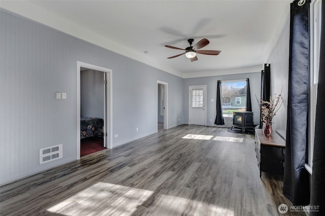 unfurnished living room featuring visible vents, baseboards, ceiling fan, a wood stove, and wood finished floors