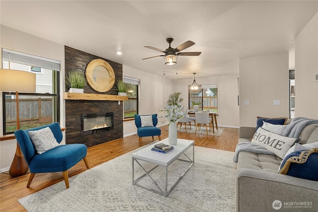 living area featuring a ceiling fan, a healthy amount of sunlight, wood finished floors, and a large fireplace