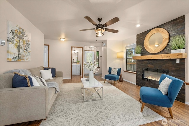 living room featuring a fireplace, wood finished floors, baseboards, and ceiling fan