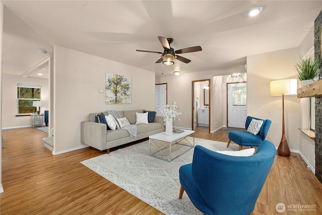 living room featuring a ceiling fan, wood finished floors, baseboards, and a fireplace with raised hearth