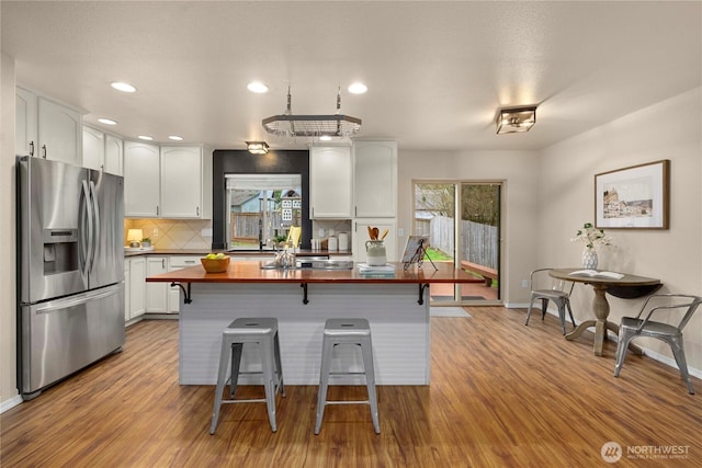 kitchen with wood counters, wood finished floors, stainless steel fridge, a breakfast bar area, and white cabinets