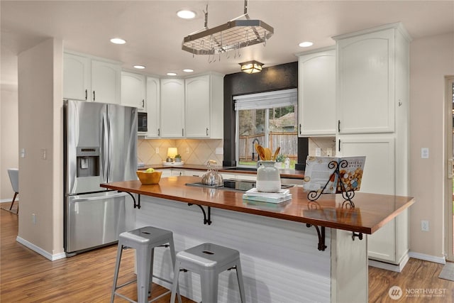 kitchen with black appliances, tasteful backsplash, wood finished floors, a breakfast bar area, and wooden counters