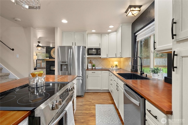 kitchen featuring ceiling fan, butcher block counters, white cabinets, stainless steel appliances, and a sink