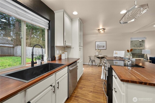 kitchen with wooden counters, light wood-style flooring, a sink, white cabinets, and appliances with stainless steel finishes