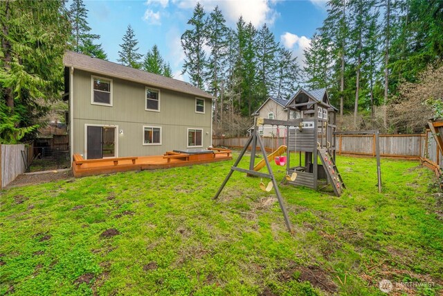 back of property featuring a playground, a yard, a fenced backyard, and a wooden deck