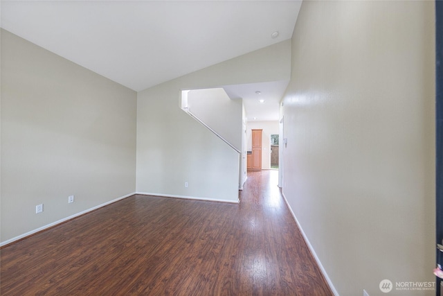 empty room featuring vaulted ceiling, dark wood-style floors, and baseboards