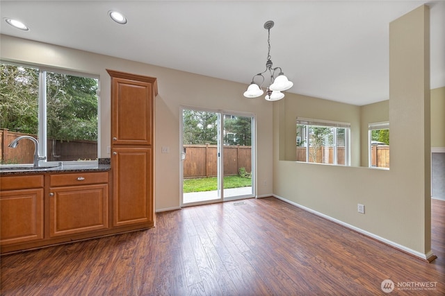 unfurnished dining area with an inviting chandelier, dark wood-style floors, baseboards, and a sink