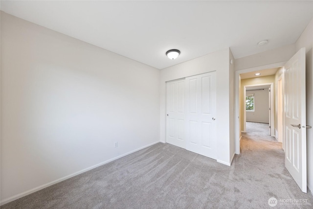 unfurnished bedroom with baseboards, light carpet, and a closet