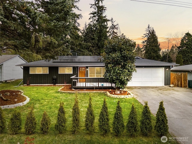 ranch-style house featuring solar panels, fence, a lawn, a garage, and driveway