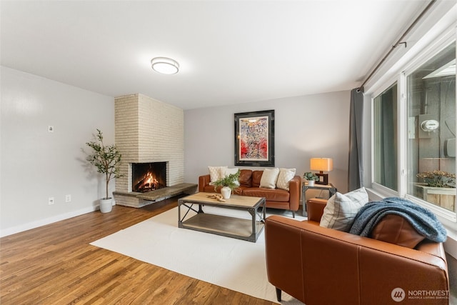 living room with baseboards, a brick fireplace, and wood finished floors