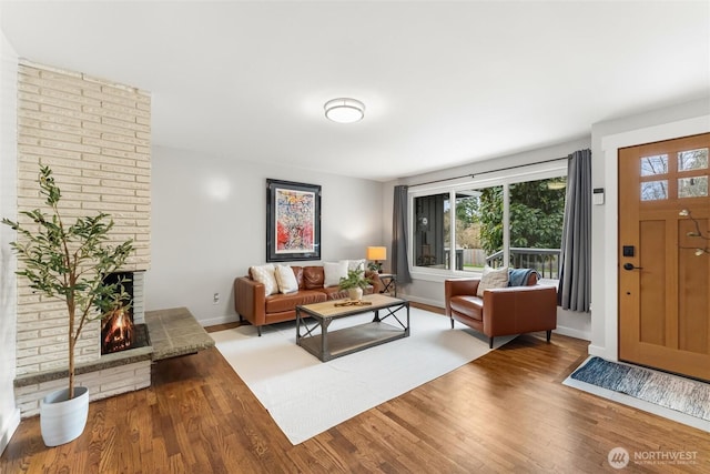 living area featuring baseboards, a brick fireplace, and wood finished floors