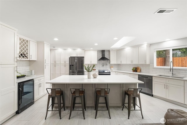 kitchen with visible vents, a sink, stainless steel appliances, wine cooler, and wall chimney exhaust hood