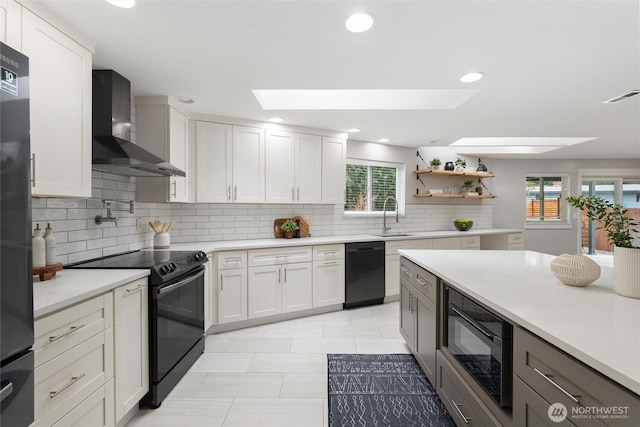 kitchen with visible vents, black appliances, a sink, a skylight, and wall chimney range hood