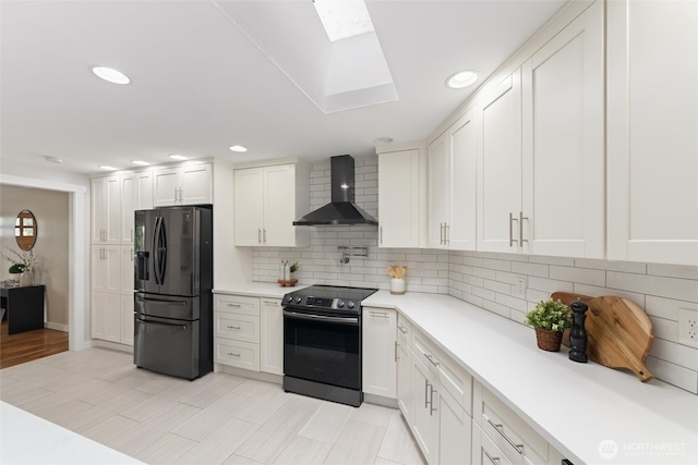 kitchen with range with electric cooktop, black fridge, wall chimney range hood, a skylight, and light countertops