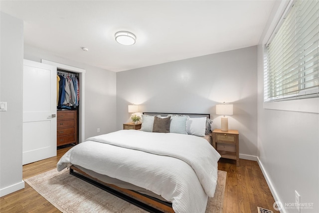 bedroom with visible vents, wood finished floors, baseboards, and a closet