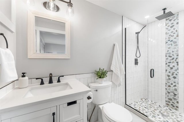 bathroom featuring tile walls, a stall shower, toilet, and vanity