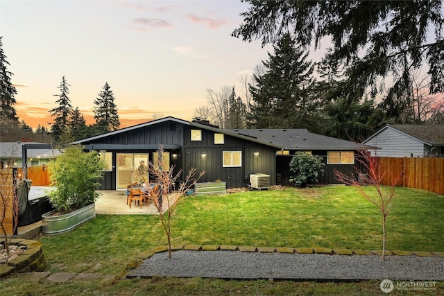 back of property with a lawn, board and batten siding, central AC unit, fence private yard, and a patio area