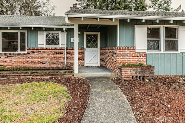 doorway to property featuring brick siding, board and batten siding, and roof with shingles