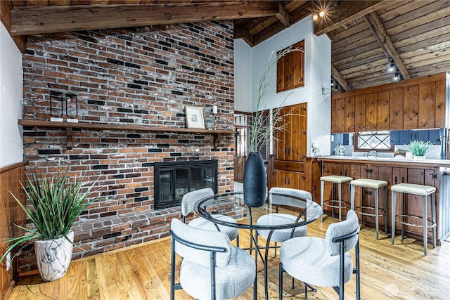 dining room featuring hardwood / wood-style flooring, a brick fireplace, wood ceiling, and beamed ceiling