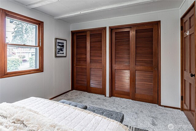 carpeted bedroom with baseboards, multiple closets, and beam ceiling