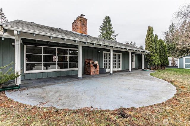 rear view of house with a shingled roof, a patio area, board and batten siding, and a chimney