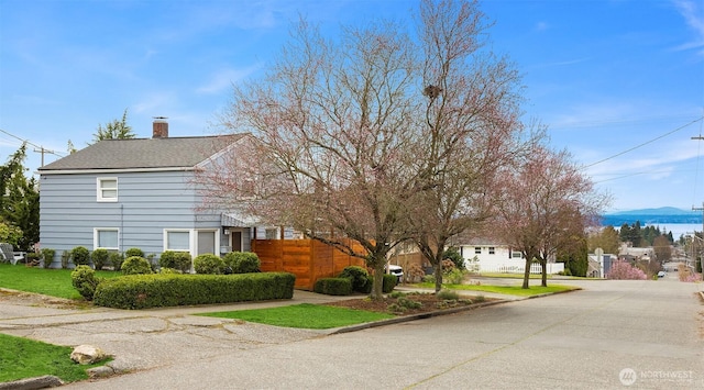 view of side of property featuring roof with shingles, a chimney, and fence